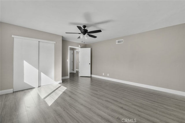 unfurnished bedroom with a ceiling fan, visible vents, wood finished floors, baseboards, and a closet