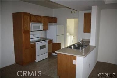kitchen featuring white appliances, a peninsula, brown cabinetry, and a sink