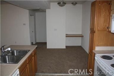 kitchen with carpet floors, light countertops, white range with electric stovetop, brown cabinets, and a sink