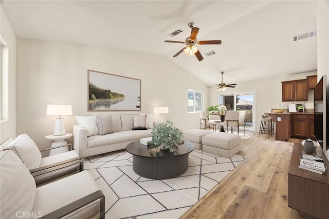 living area featuring a ceiling fan, lofted ceiling, light wood-style flooring, and visible vents