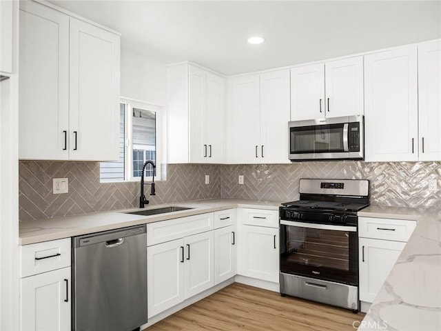 kitchen featuring white cabinets, stainless steel appliances, light stone countertops, and a sink