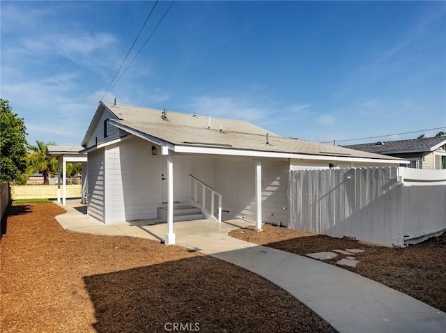 rear view of house featuring fence and roof with shingles