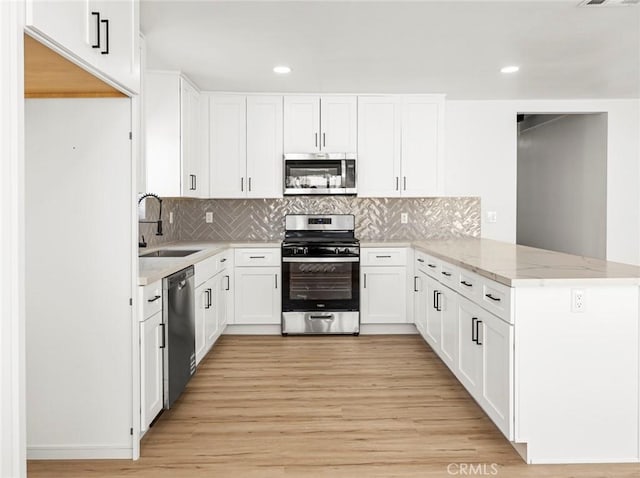 kitchen featuring light stone countertops, a sink, light wood-style floors, stainless steel appliances, and a peninsula