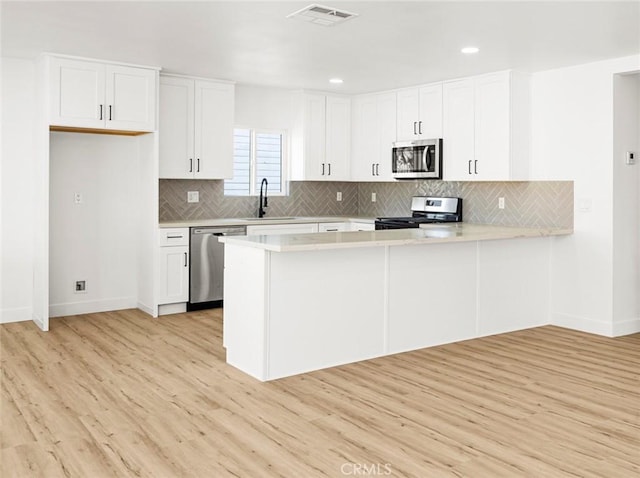 kitchen featuring visible vents, a peninsula, light wood-style floors, light countertops, and appliances with stainless steel finishes