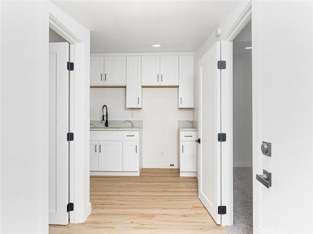 interior space with light wood-type flooring, recessed lighting, white cabinetry, light countertops, and a sink