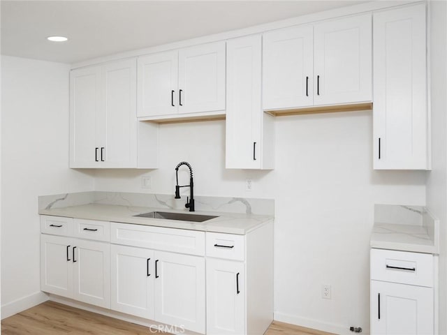 kitchen with light stone countertops, baseboards, white cabinets, a sink, and light wood finished floors