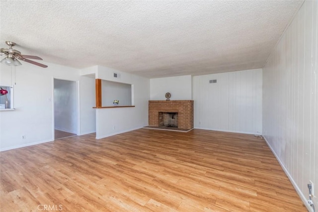 unfurnished living room with a fireplace, ceiling fan, light wood-style flooring, and a textured ceiling