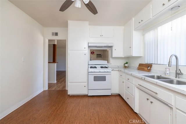 kitchen with a sink, wood finished floors, visible vents, under cabinet range hood, and white range with gas stovetop
