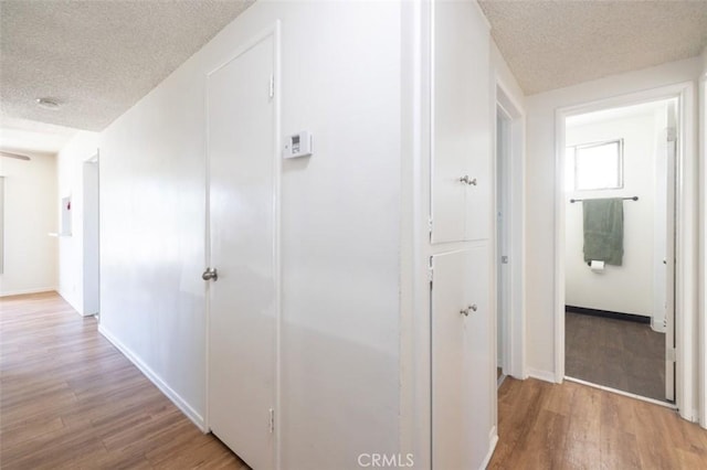 hall with a textured ceiling, baseboards, and wood finished floors
