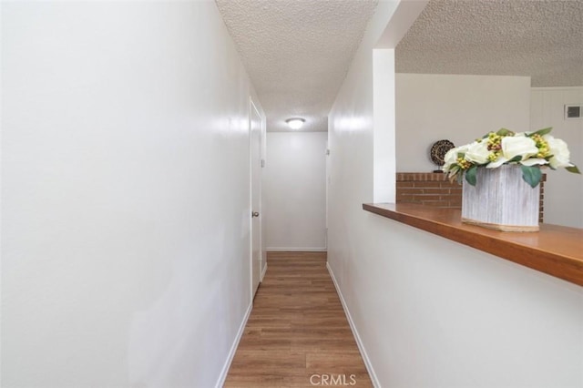 corridor with a textured ceiling, baseboards, visible vents, and light wood-style floors