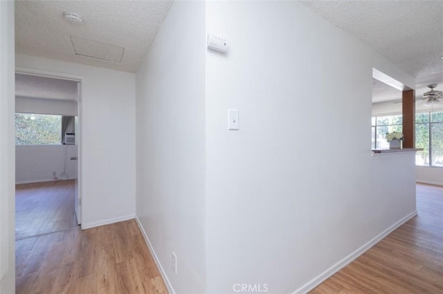 hallway with attic access, a textured ceiling, wood finished floors, and baseboards