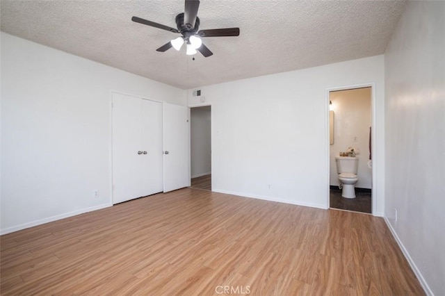 unfurnished bedroom with a textured ceiling, ensuite bathroom, baseboards, visible vents, and light wood-style floors