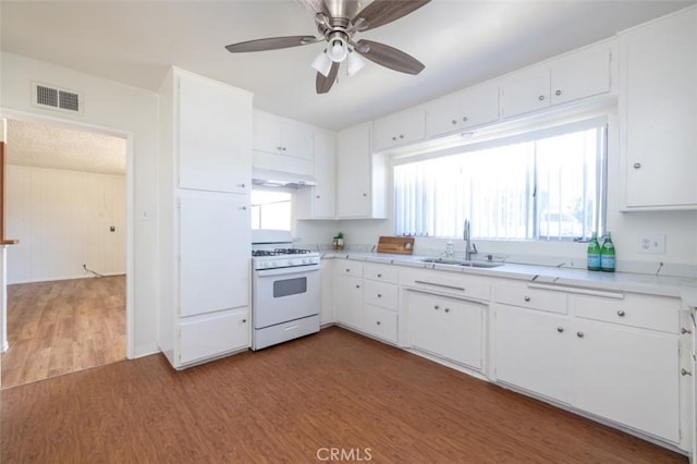 kitchen with white range with gas stovetop, wood finished floors, a sink, white cabinets, and visible vents