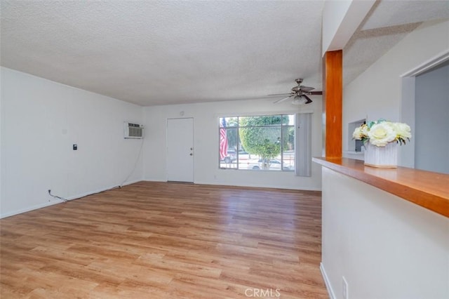 unfurnished living room featuring a textured ceiling, ceiling fan, light wood-style flooring, an AC wall unit, and baseboards