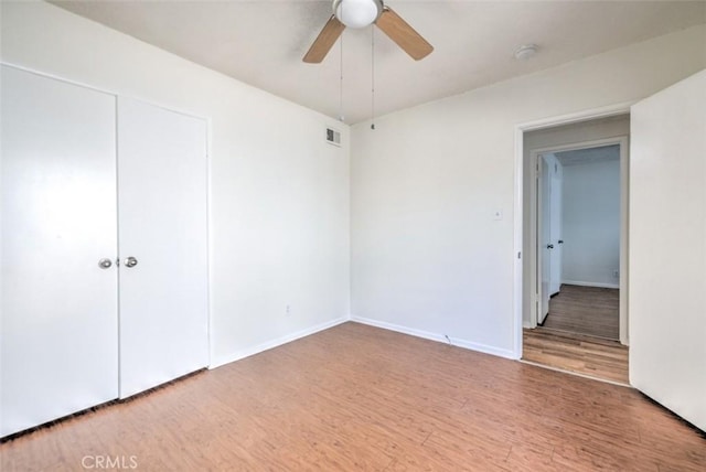 unfurnished bedroom with a closet, wood finished floors, visible vents, a ceiling fan, and baseboards
