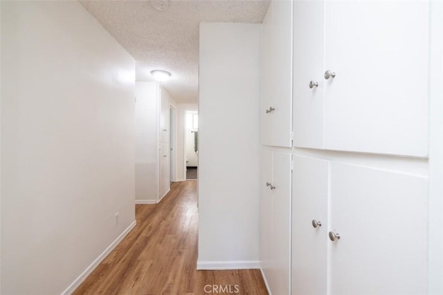 hall with a textured ceiling, baseboards, and light wood-style floors