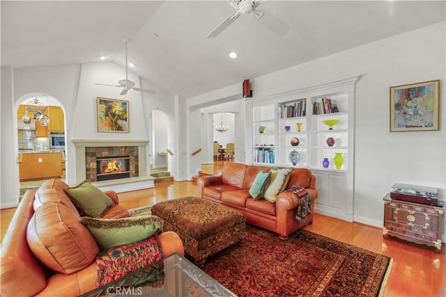 living room with arched walkways, vaulted ceiling, wood finished floors, and ceiling fan with notable chandelier