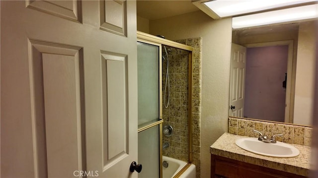 full bath featuring shower / bath combination with glass door, a textured wall, and vanity