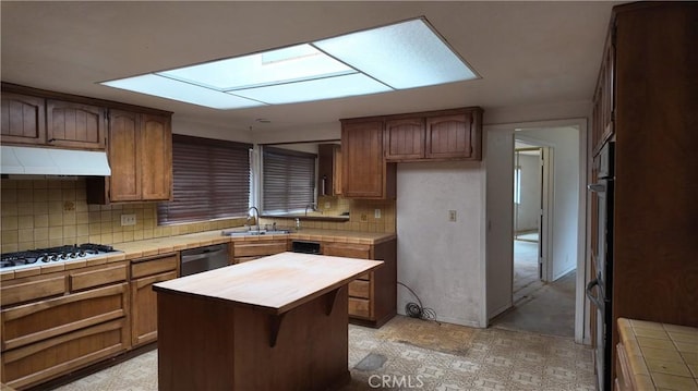 kitchen featuring under cabinet range hood, tile counters, tasteful backsplash, and gas stovetop