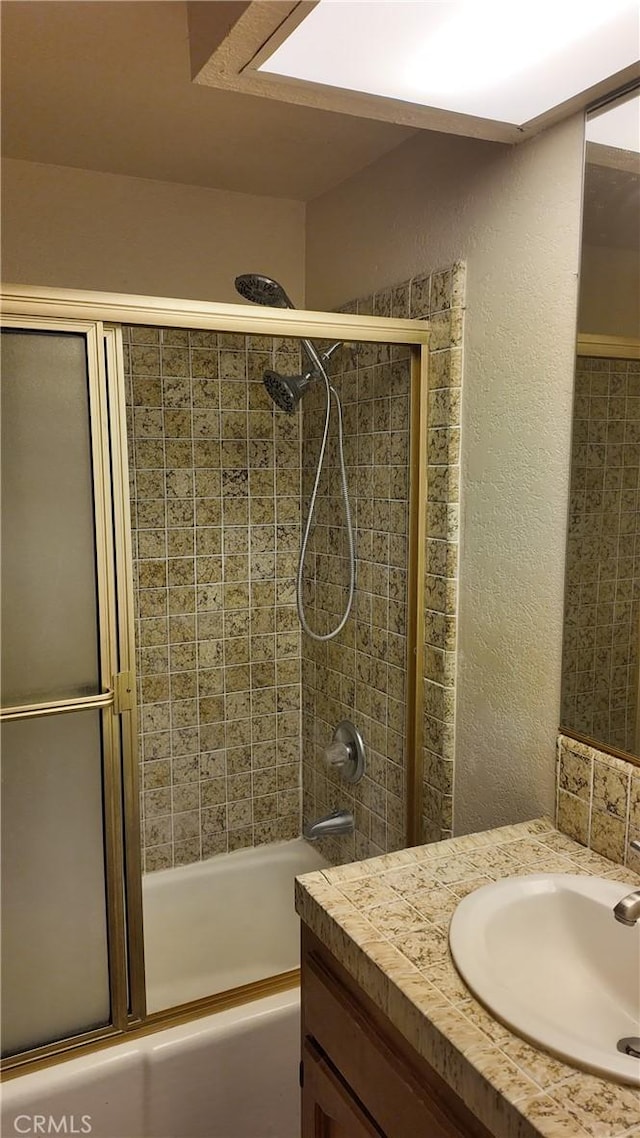 bathroom with vanity, a textured wall, and combined bath / shower with glass door