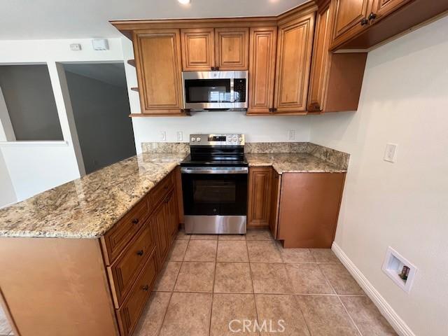 14675 Red Hill Ave, Tustin, CA 92780 - kitchen featuring a peninsula, baseboards, brown cabinets, light stone counters, and stainless steel appliances