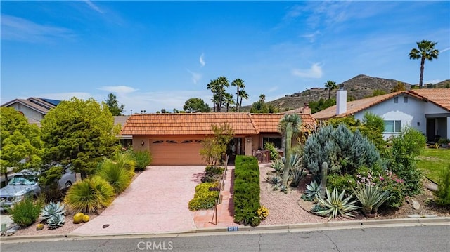 view of front of house with driveway, a tile roof, a mountain view, an attached garage, and stucco siding