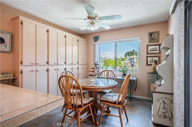 dining area featuring baseboards, a ceiling fan, and a textured ceiling