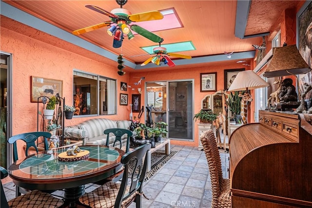 dining area featuring stone tile floors, a ceiling fan, a skylight, and wood ceiling