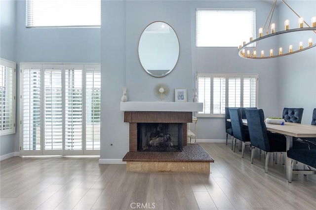 living area featuring a brick fireplace, wood finished floors, baseboards, a chandelier, and a high ceiling