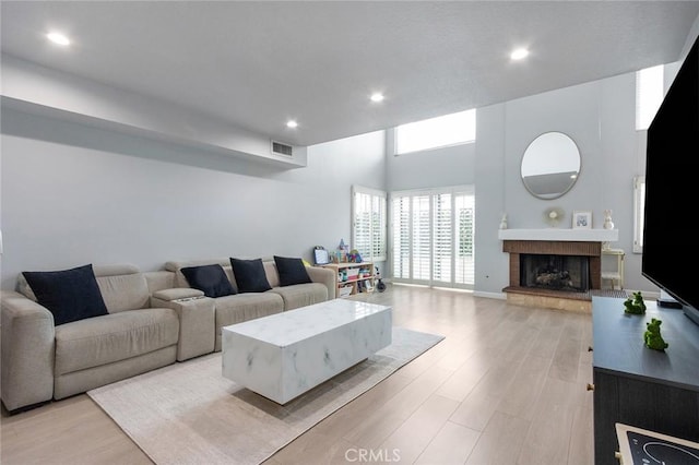 living room with recessed lighting, visible vents, a fireplace with raised hearth, and light wood-style floors
