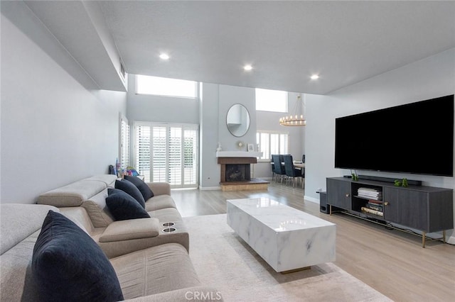 living room with light wood-style floors, recessed lighting, a fireplace with raised hearth, and a notable chandelier