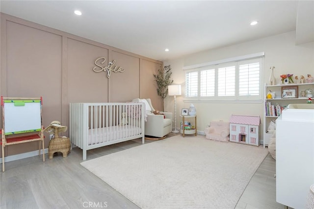 bedroom with a nursery area, recessed lighting, and wood finished floors