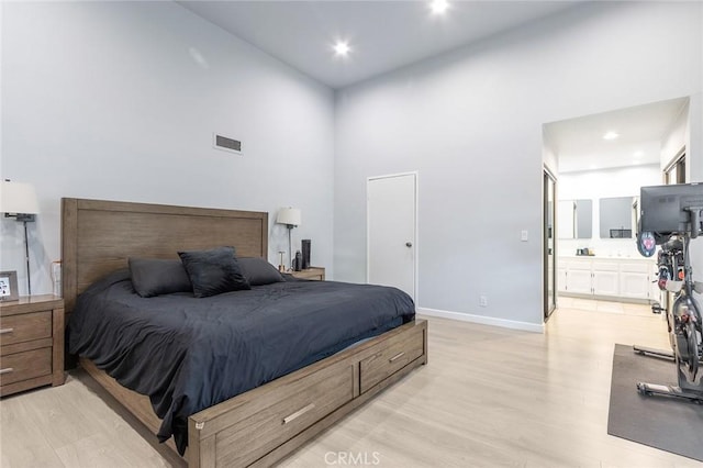 bedroom with visible vents, light wood-type flooring, baseboards, a high ceiling, and ensuite bath