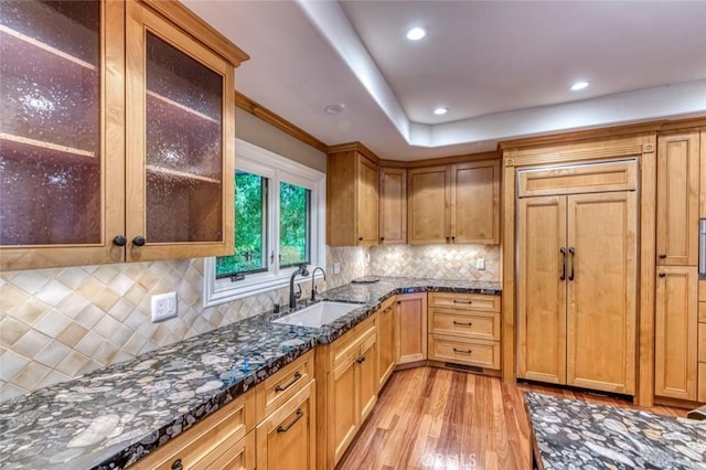 kitchen with a sink, light wood-style floors, backsplash, and dark stone countertops
