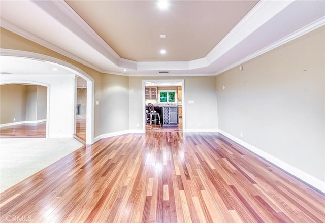 unfurnished room featuring arched walkways, baseboards, a raised ceiling, and light wood-style floors