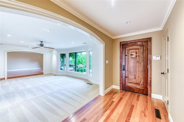 foyer entrance with crown molding, ceiling fan, arched walkways, baseboards, and visible vents