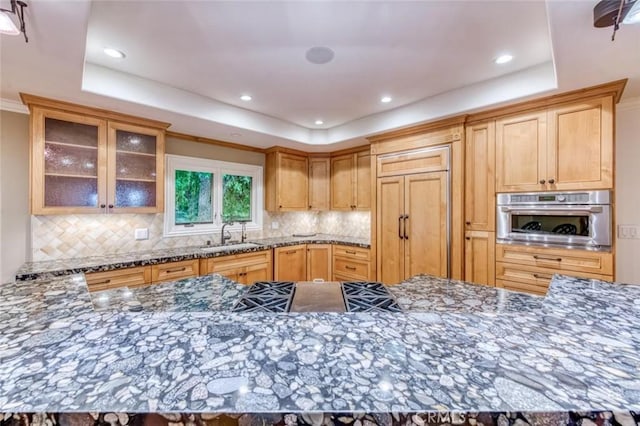 kitchen with decorative backsplash, a sink, dark stone countertops, a tray ceiling, and oven