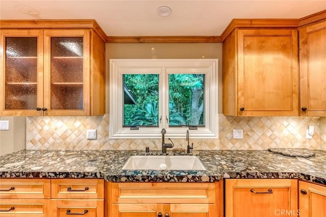 kitchen with dark stone counters, glass insert cabinets, decorative backsplash, and a sink