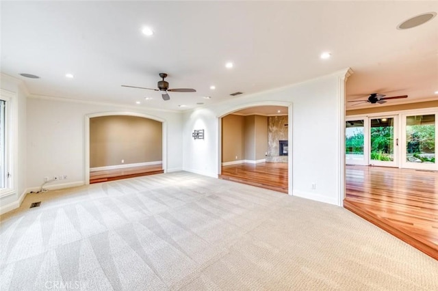 unfurnished living room with baseboards, light colored carpet, recessed lighting, arched walkways, and a ceiling fan