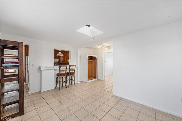 spare room with light tile patterned flooring, a skylight, and baseboards