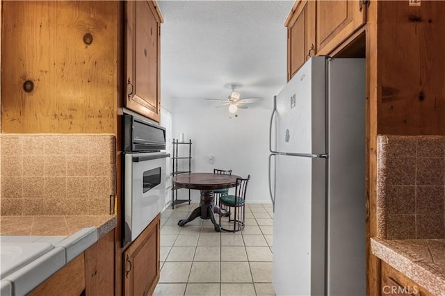 kitchen with brown cabinets, stainless steel oven, freestanding refrigerator, a ceiling fan, and light tile patterned floors