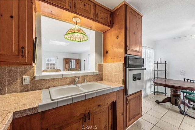 kitchen featuring brown cabinets, a sink, stainless steel oven, decorative backsplash, and light tile patterned floors