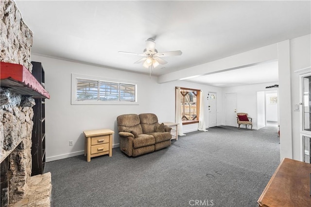 living room with carpet flooring, a ceiling fan, baseboards, and a stone fireplace