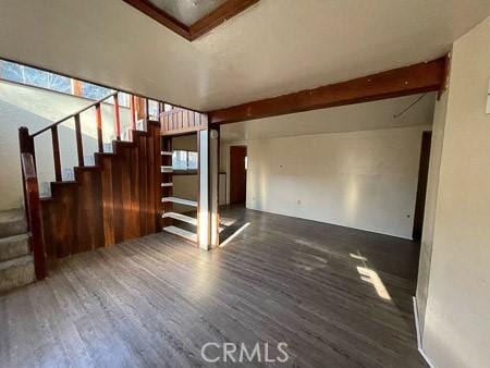 unfurnished living room with stairs, beamed ceiling, and wood finished floors