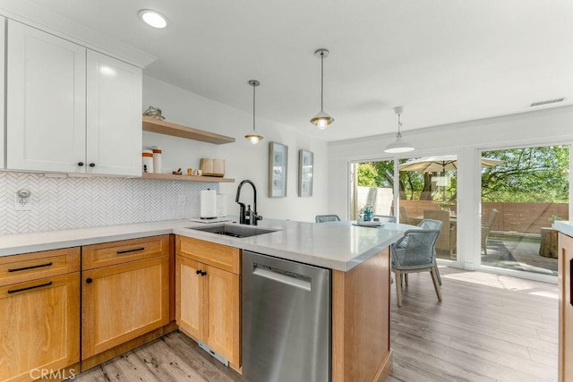 kitchen featuring open shelves, a sink, light wood finished floors, dishwasher, and a peninsula
