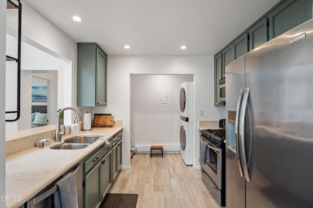kitchen with appliances with stainless steel finishes, a sink, recessed lighting, stacked washer / dryer, and light wood-type flooring