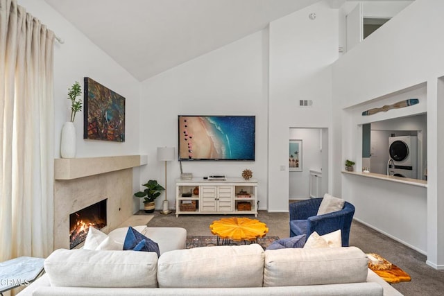 living area with visible vents, high vaulted ceiling, carpet, stacked washer / drying machine, and a premium fireplace