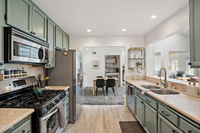kitchen featuring appliances with stainless steel finishes, a sink, light countertops, green cabinets, and light wood finished floors