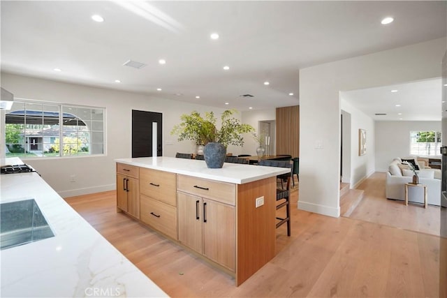 kitchen featuring light brown cabinetry, recessed lighting, open floor plan, and light wood-style flooring