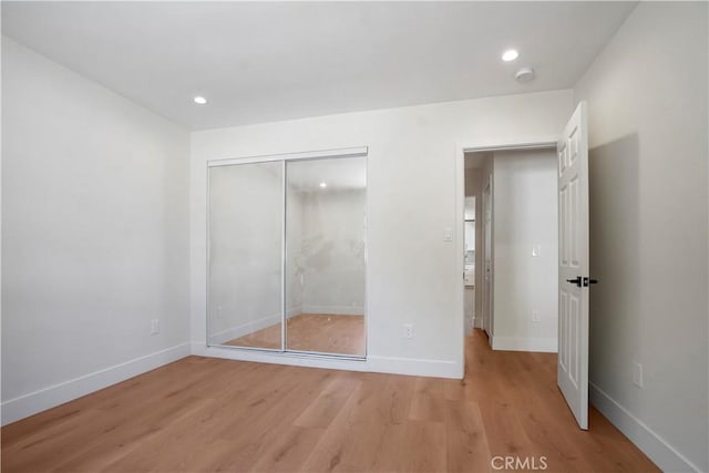 unfurnished bedroom with light wood-type flooring, baseboards, and a closet
